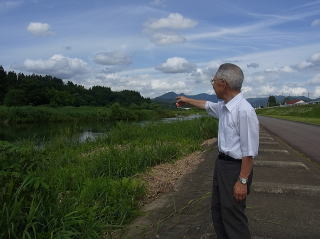 川を指さす沼沢さんの写真